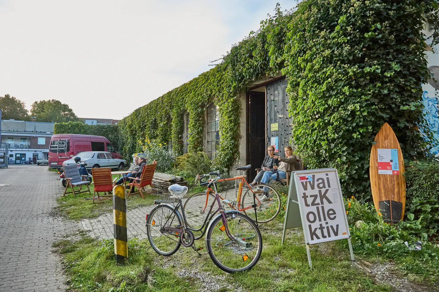 Efeubewachsene Werkstatt des Waitz-Kollektivs am Knooper Weg, davor Fahrräder, Liegestühle und ein Surfbrett aus Holz